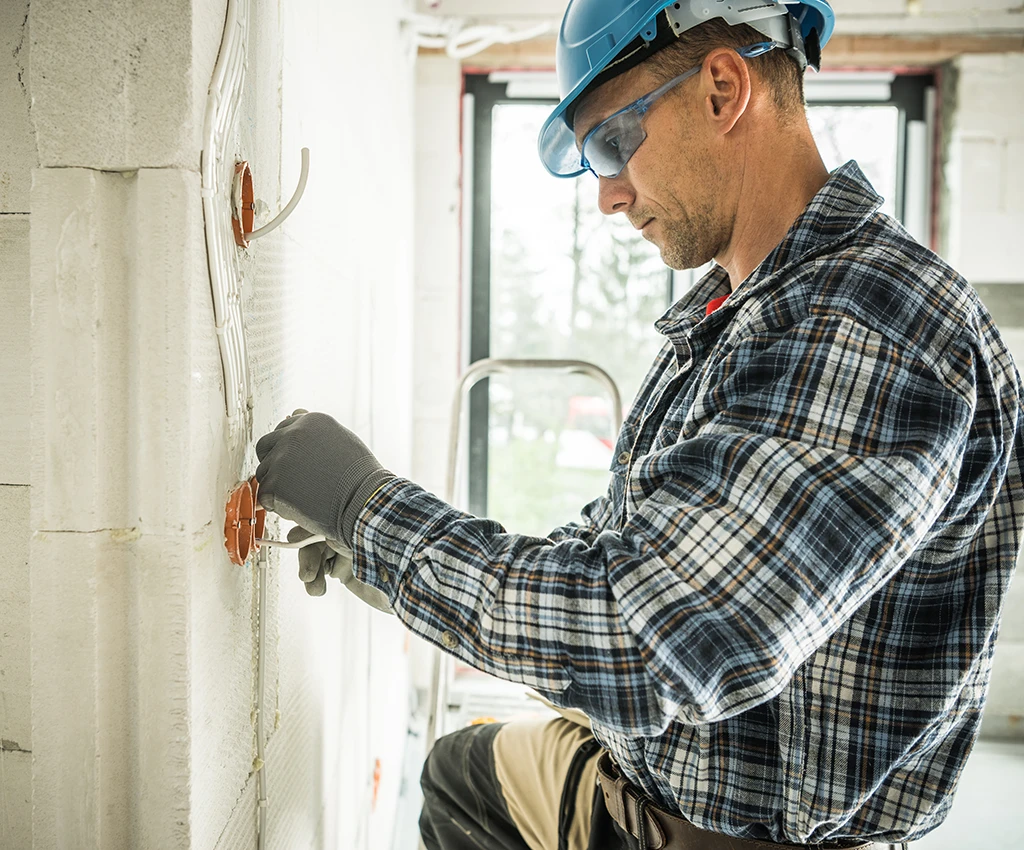 Professional Electrician in Safety Equipment Installing Electrical Wiring System in Freshly Built Residential House.