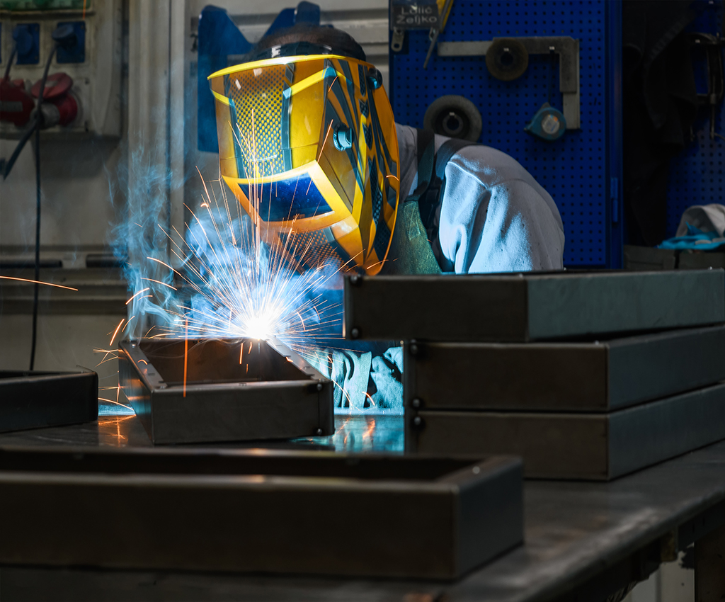 Professional welder performs work with metal parts in factory, sparks, and electricity.