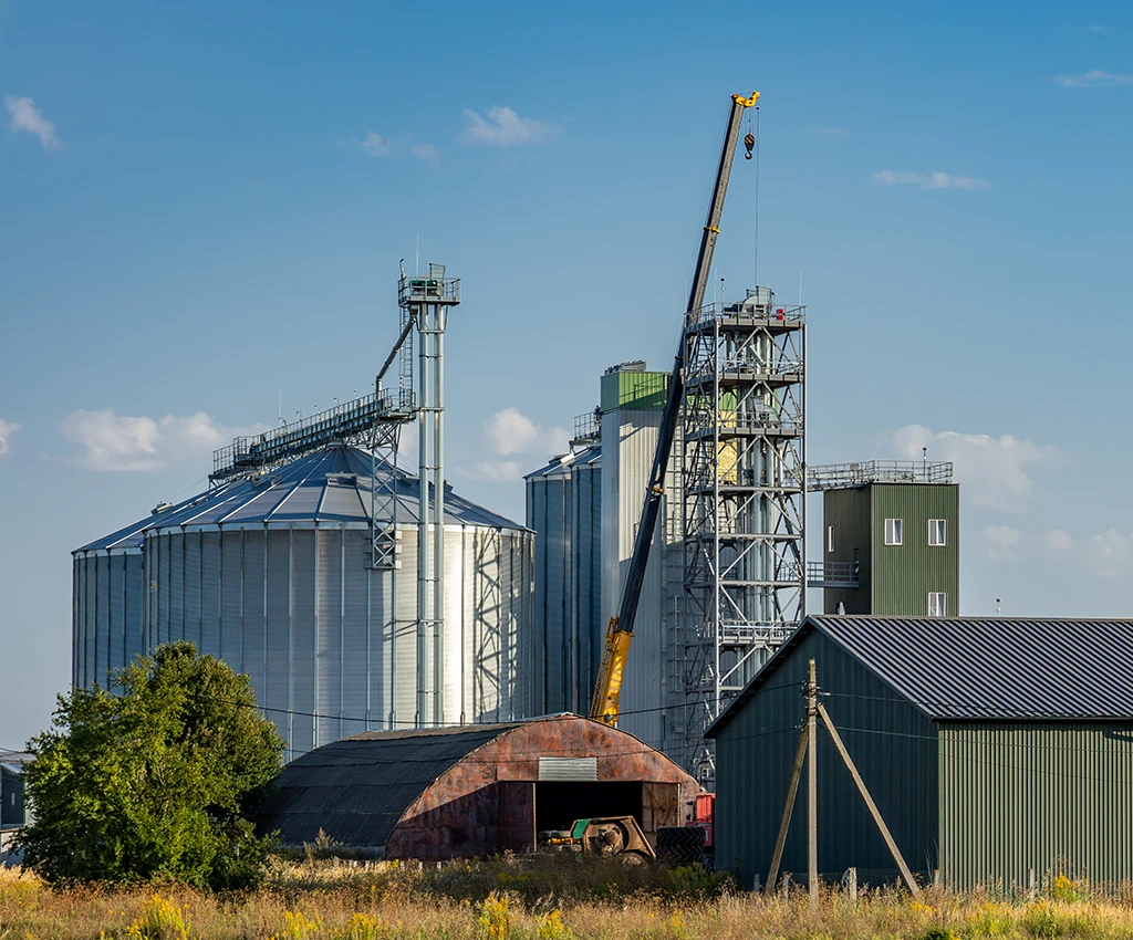 Construction crane stands next to grain silos and a barn.